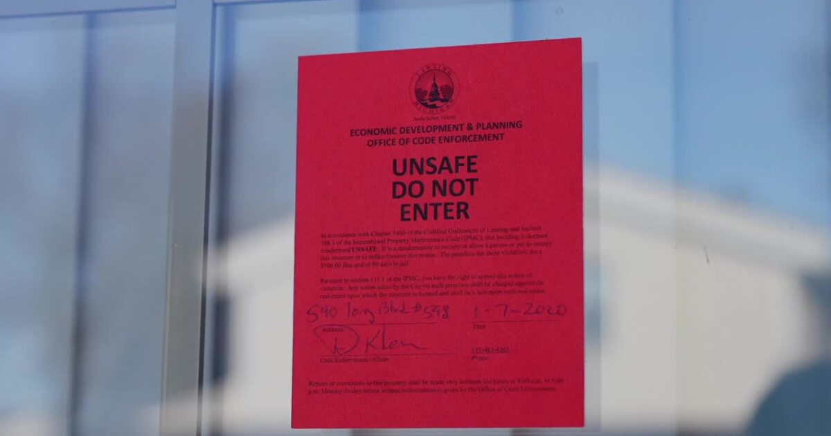A red Unsafe Do Not Enter sign with the city of Lansing seal, taped to a window.